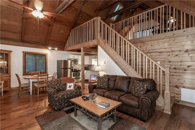 living room with a ceiling fan, wood finished floors, high vaulted ceiling, beam ceiling, and stairs