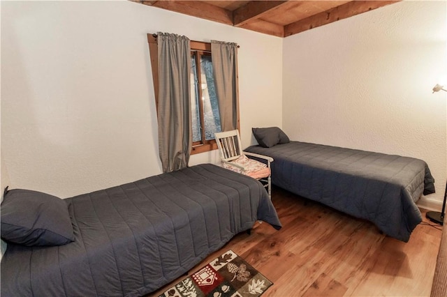 bedroom with beam ceiling and wood finished floors