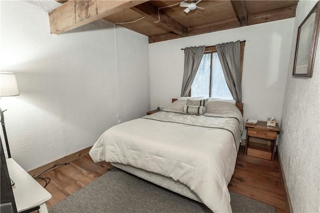 bedroom featuring beam ceiling, a textured wall, and wood finished floors