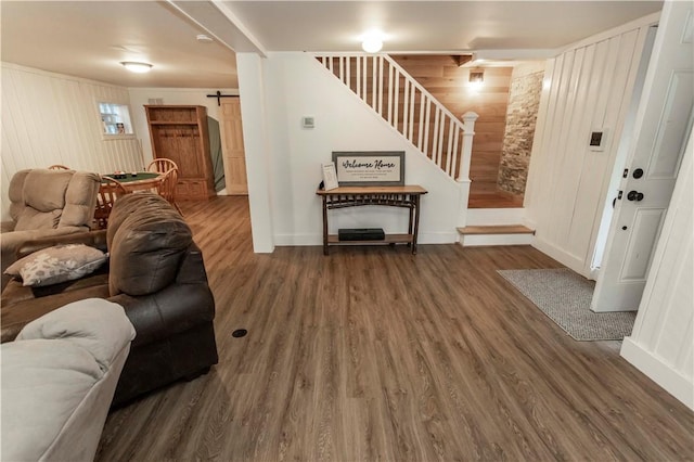 living area with wooden walls, baseboards, stairs, a barn door, and wood finished floors