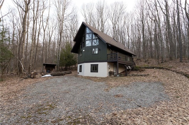 view of side of home with a deck, driveway, and roof with shingles