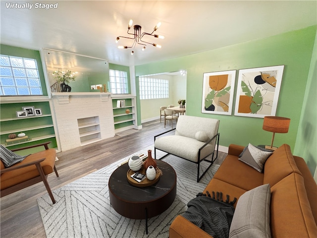 living room featuring a notable chandelier, a brick fireplace, baseboards, and wood finished floors