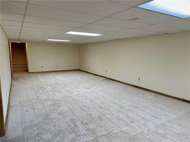 carpeted empty room with stairs, baseboards, and a drop ceiling