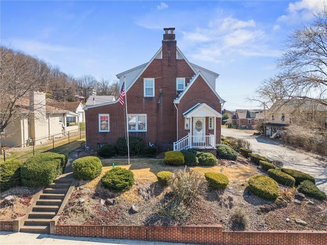 view of front facade with brick siding, a chimney, and fence