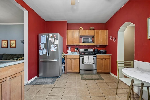 kitchen featuring baseboards, light countertops, light tile patterned floors, arched walkways, and stainless steel appliances