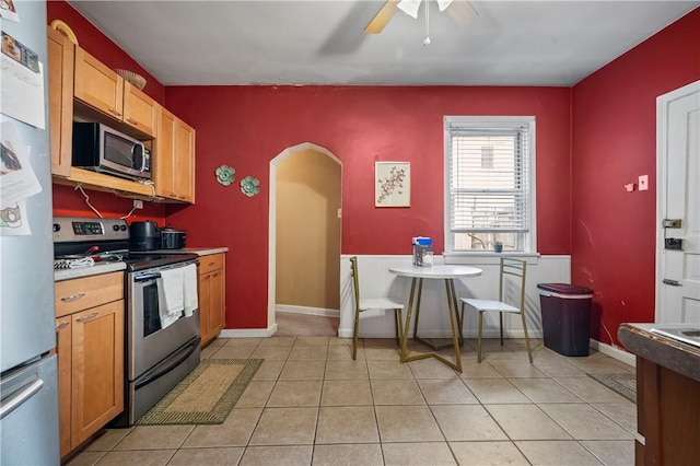 kitchen with arched walkways, light tile patterned floors, appliances with stainless steel finishes, and a ceiling fan