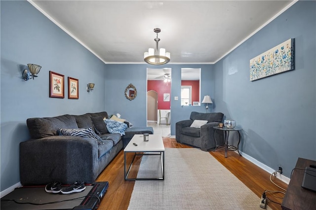 living room featuring arched walkways, crown molding, baseboards, and wood finished floors