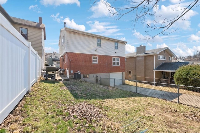 rear view of house featuring central air condition unit, a fenced backyard, concrete driveway, an attached garage, and brick siding