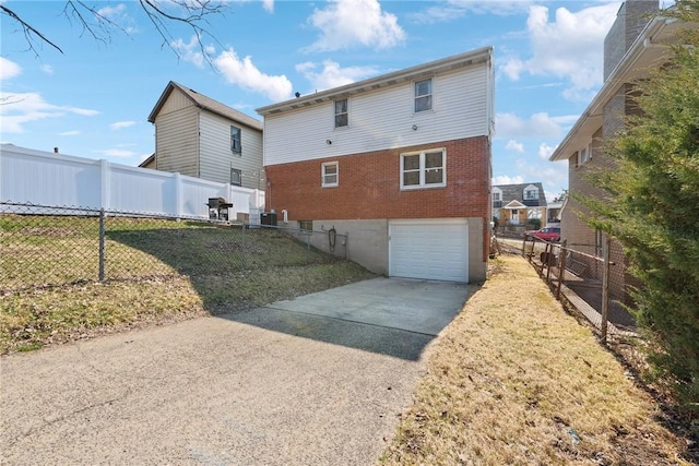 rear view of property with fence, concrete driveway, a garage, a lawn, and brick siding