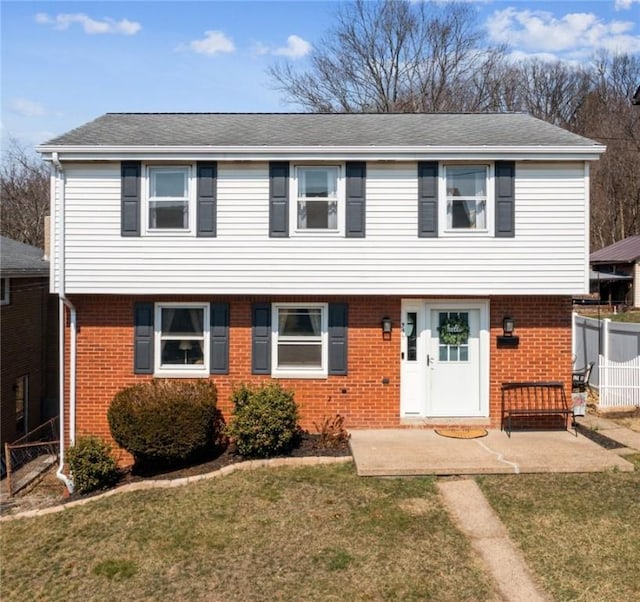 colonial inspired home with a patio, brick siding, a front yard, and fence