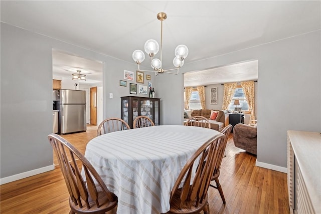 dining area featuring an inviting chandelier, baseboards, and light wood-style floors