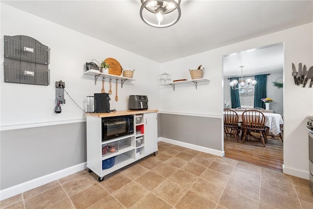 interior space featuring baseboards, black microwave, a chandelier, light countertops, and open shelves