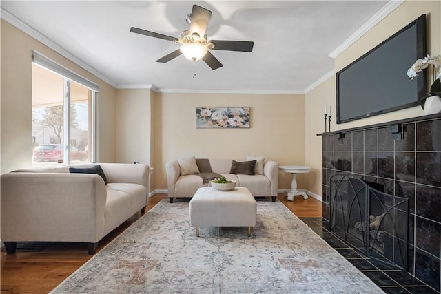 living room with baseboards, dark wood-style flooring, ceiling fan, ornamental molding, and a tiled fireplace