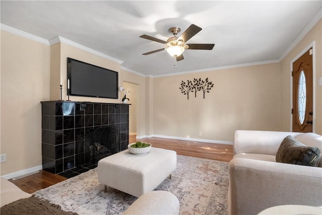 living area featuring a fireplace, crown molding, baseboards, and wood finished floors