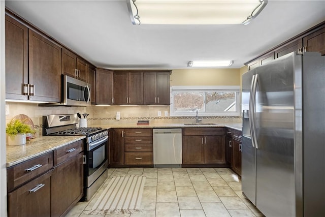 kitchen with a sink, stainless steel appliances, light stone countertops, and tasteful backsplash