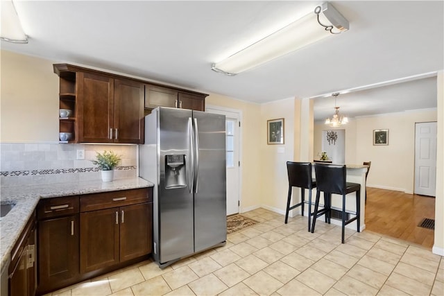 kitchen featuring light stone countertops, dark brown cabinetry, decorative backsplash, stainless steel refrigerator with ice dispenser, and open shelves