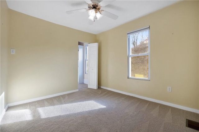 carpeted spare room with baseboards, visible vents, and ceiling fan