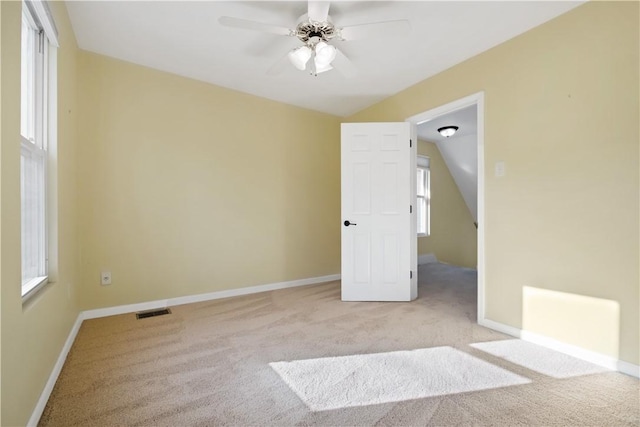 carpeted empty room with vaulted ceiling, baseboards, visible vents, and ceiling fan