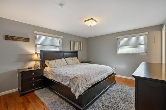 bedroom with multiple windows, wood finished floors, and baseboards