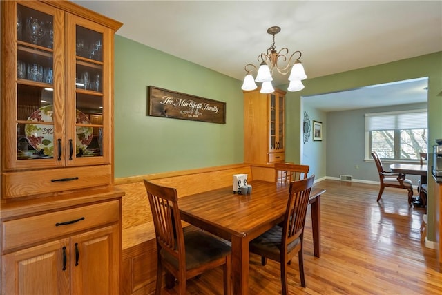 dining area featuring light wood-style flooring, baseboards, visible vents, and a chandelier