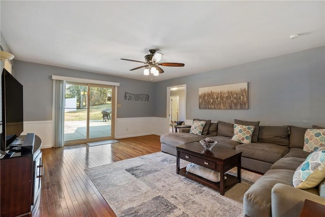 living area featuring a wainscoted wall, wood-type flooring, and a ceiling fan