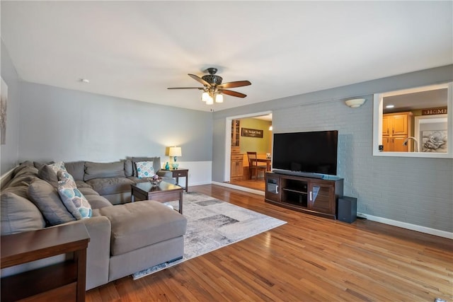 living room featuring a ceiling fan, wood finished floors, baseboards, and brick wall