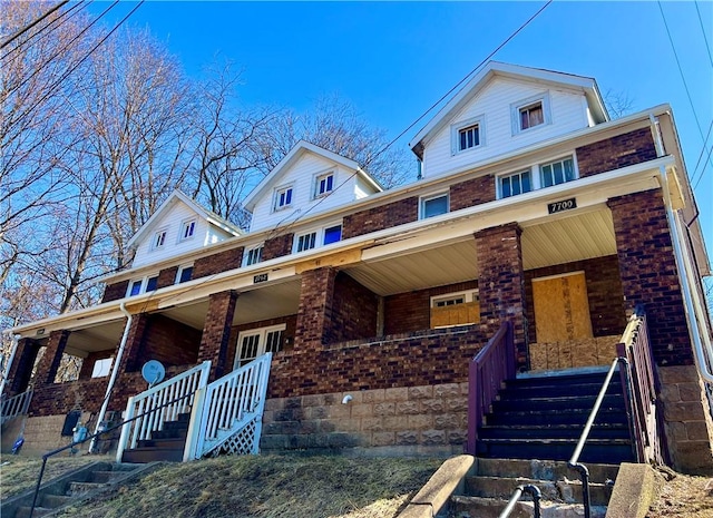 view of front of house with stairway, brick siding, and covered porch