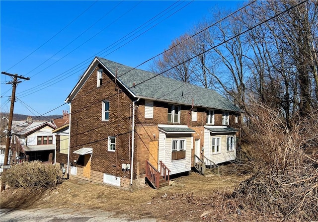 view of side of home with entry steps, brick siding, and a shingled roof