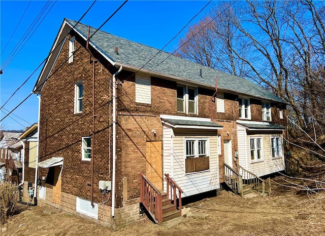 view of side of property with entry steps, brick siding, and a shingled roof