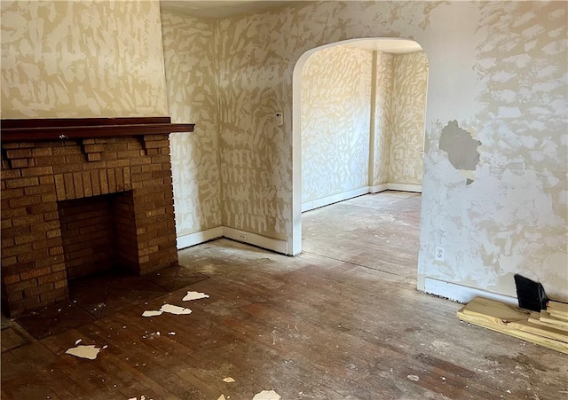 unfurnished living room featuring a brick fireplace, wallpapered walls, baseboards, and wood finished floors