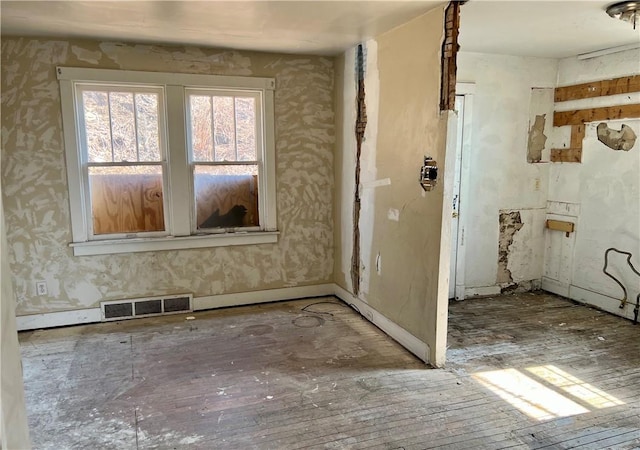 spare room featuring wallpapered walls, visible vents, baseboards, and hardwood / wood-style flooring