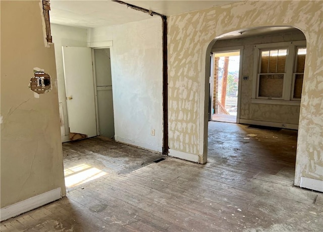 empty room with arched walkways and hardwood / wood-style floors