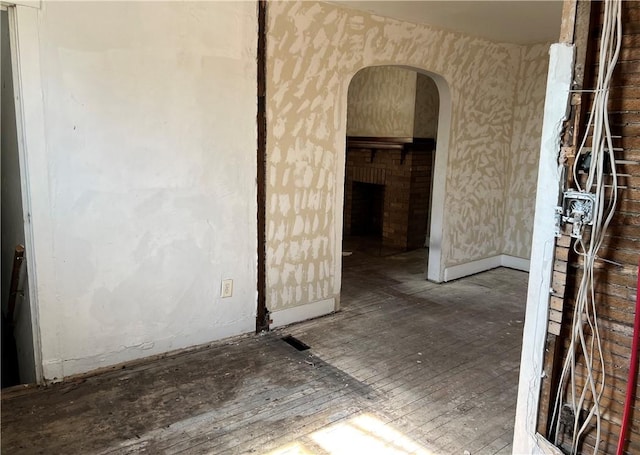 unfurnished room with arched walkways, hardwood / wood-style flooring, a brick fireplace, and wallpapered walls