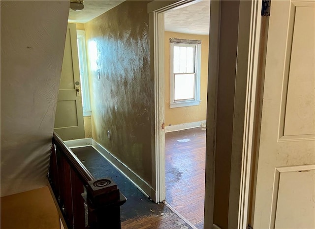 hall with dark wood finished floors, a textured wall, and baseboards