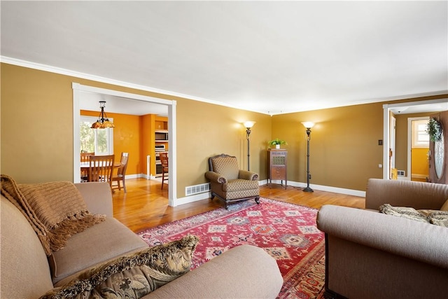 living room with visible vents, crown molding, baseboards, and wood finished floors