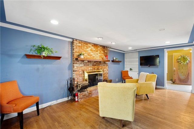 living area featuring baseboards, a brick fireplace, wood finished floors, and crown molding