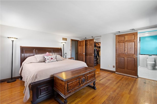 bedroom with baseboards, light wood finished floors, ensuite bath, a closet, and a barn door