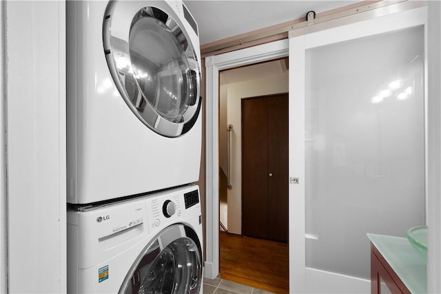 clothes washing area featuring light tile patterned floors, stacked washer / drying machine, a barn door, and laundry area