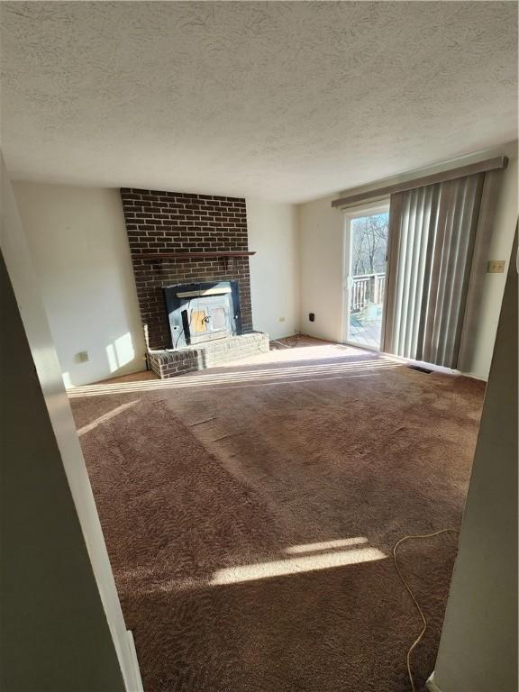 unfurnished living room with carpet flooring, a textured ceiling, and a wood stove