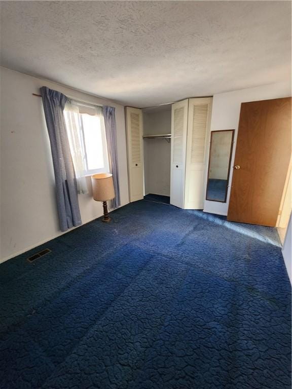 unfurnished bedroom featuring visible vents, dark carpet, and a textured ceiling