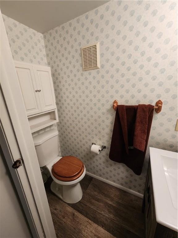 bathroom featuring visible vents, wallpapered walls, baseboards, toilet, and wood finished floors