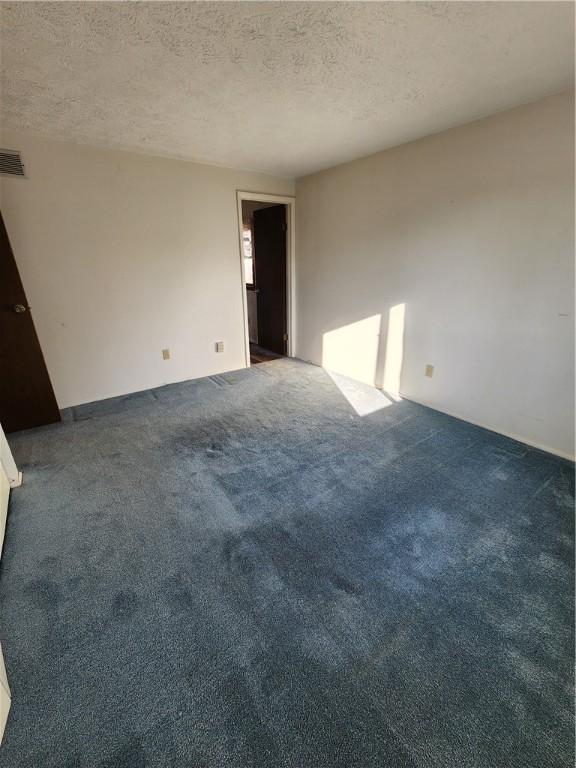 empty room featuring visible vents, dark carpet, and a textured ceiling