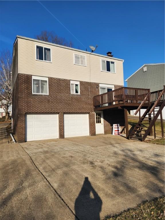 back of house featuring concrete driveway, stairway, a garage, and brick siding