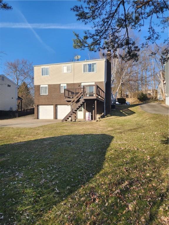 rear view of house featuring stairway, driveway, an attached garage, a chimney, and a lawn