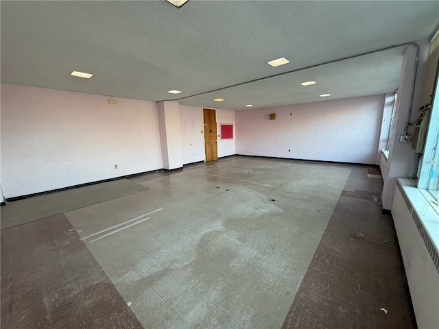 spare room with tile patterned floors, concrete block wall, radiator heating unit, and a textured ceiling