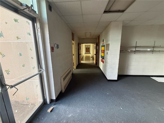 hall with visible vents, concrete block wall, and a paneled ceiling