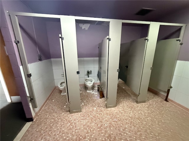 bathroom featuring visible vents, toilet, and tile walls