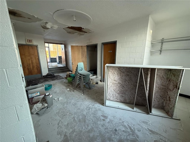 miscellaneous room featuring unfinished concrete flooring, a textured ceiling, and concrete block wall