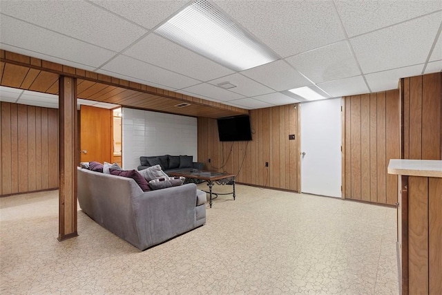 living room featuring wooden walls, light floors, and a paneled ceiling