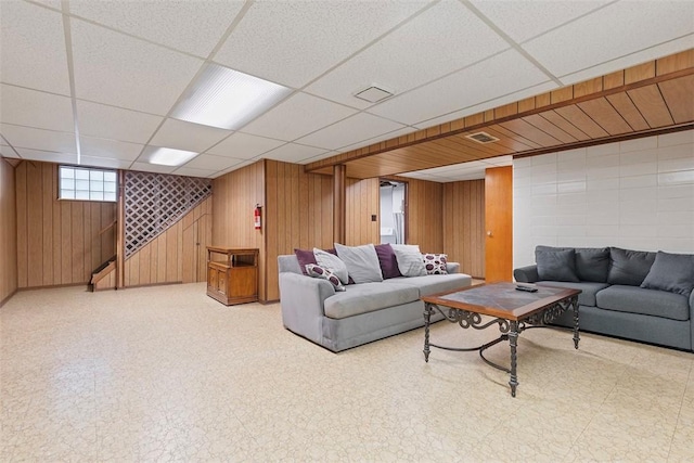 living area featuring visible vents, wooden walls, stairway, tile patterned floors, and a paneled ceiling